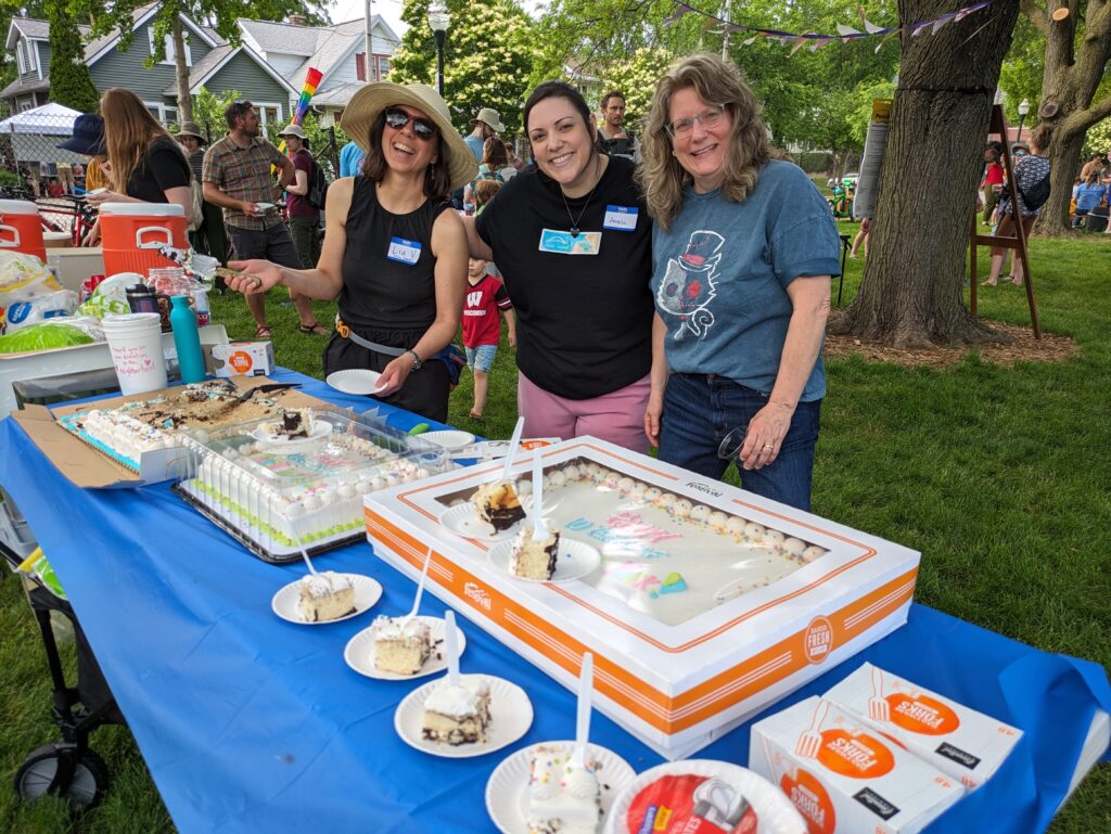 three women stand next to cakes at with tree behind them